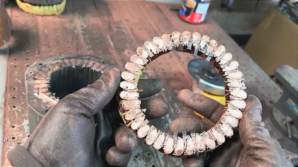 Gloved hands holding a circular copper motor winding removed from a stator
