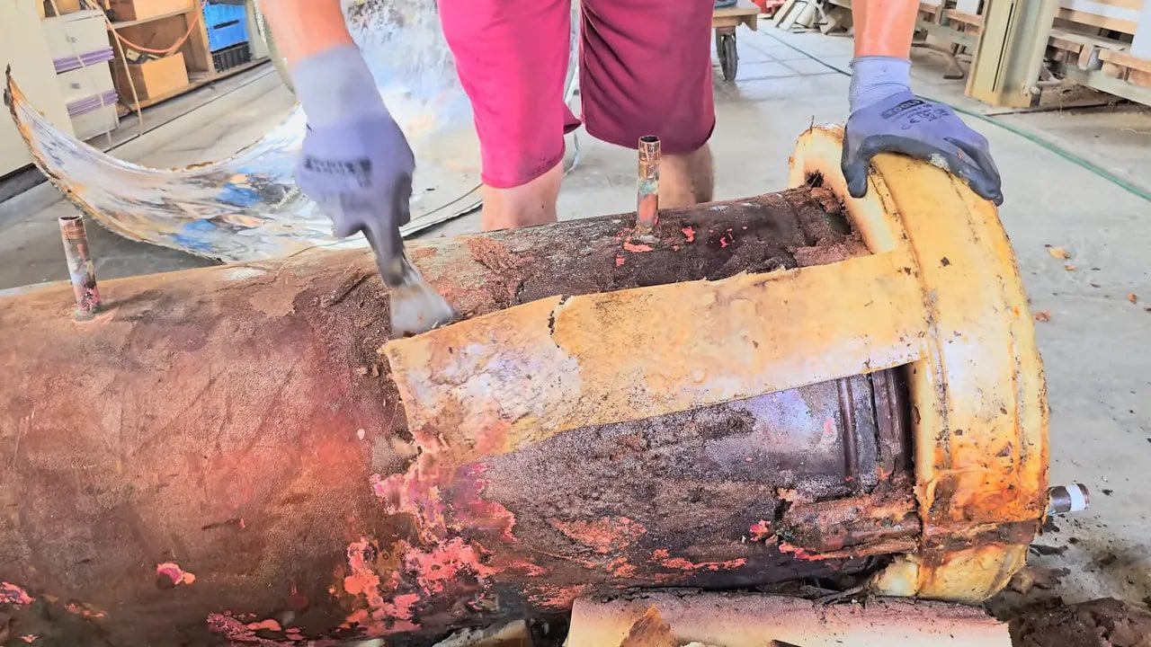Large corroded copper water heater tank lying on the ground with text identifying it as 100 percent copper