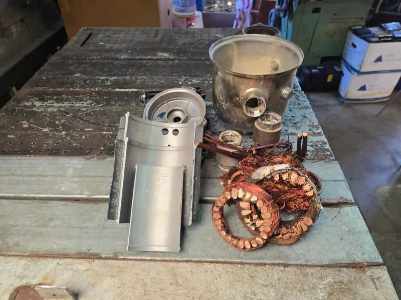 Copper windings, cut motor housing sections, pump casing, and threaded fittings arranged on a workbench after dismantling.